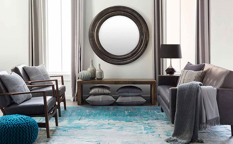 Living room with grey chairs, sofa and blue ottoman on a blue rug.